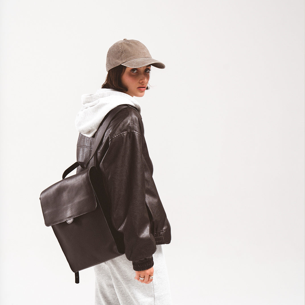 Leather backpack for woman stylishly carried by a young woman in a casual outfit with a cap and leather jacket, highlighting the backpack's sleek design and practicality