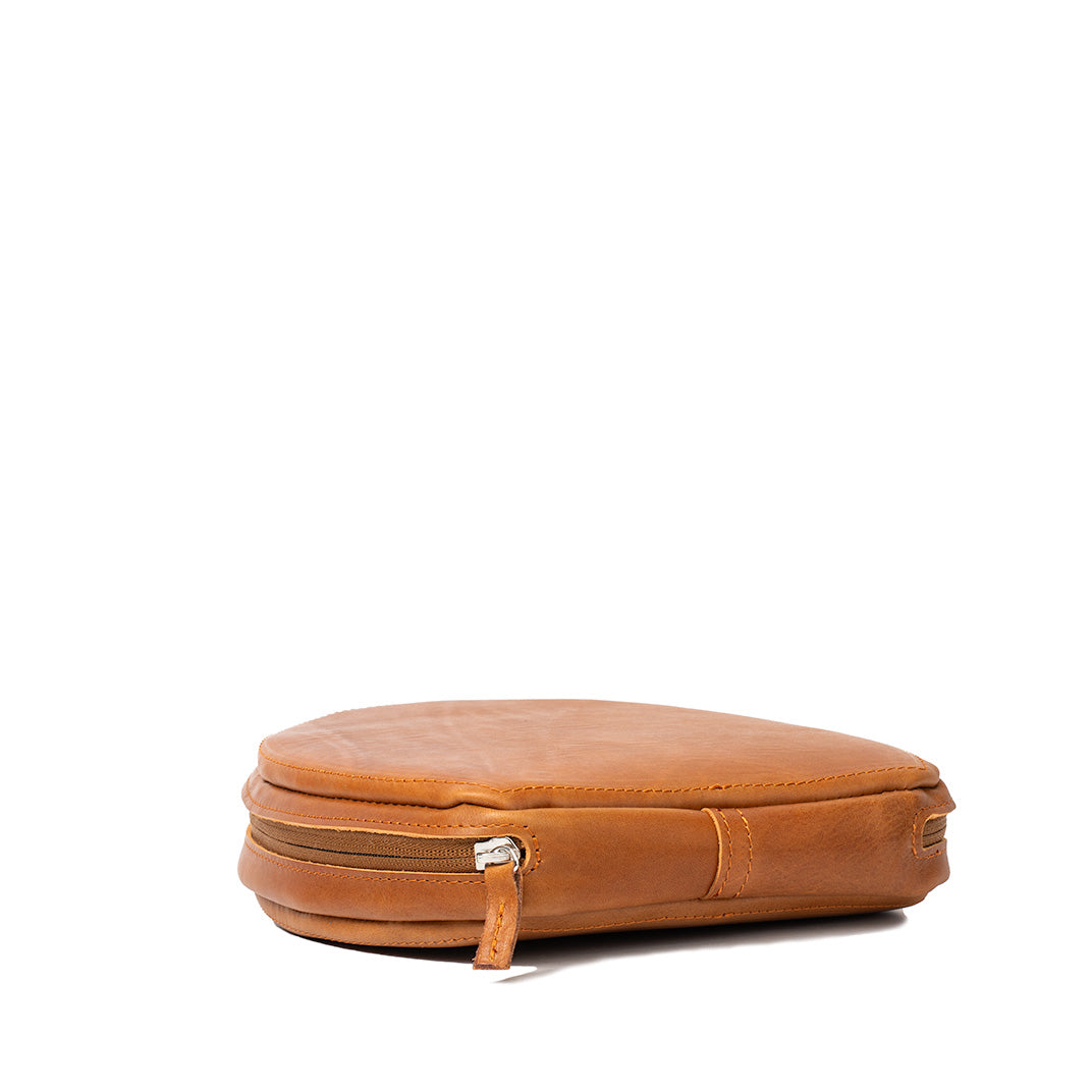 Closed AirPods Max case in Tan leather by Geometric Goods, showing zipper closure, rounded shape, and strap loop detail