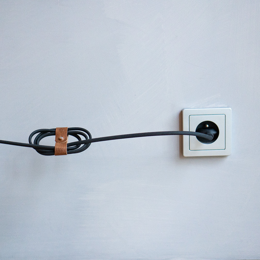 Leather cable holder securing a power cord plugged into a wall socket