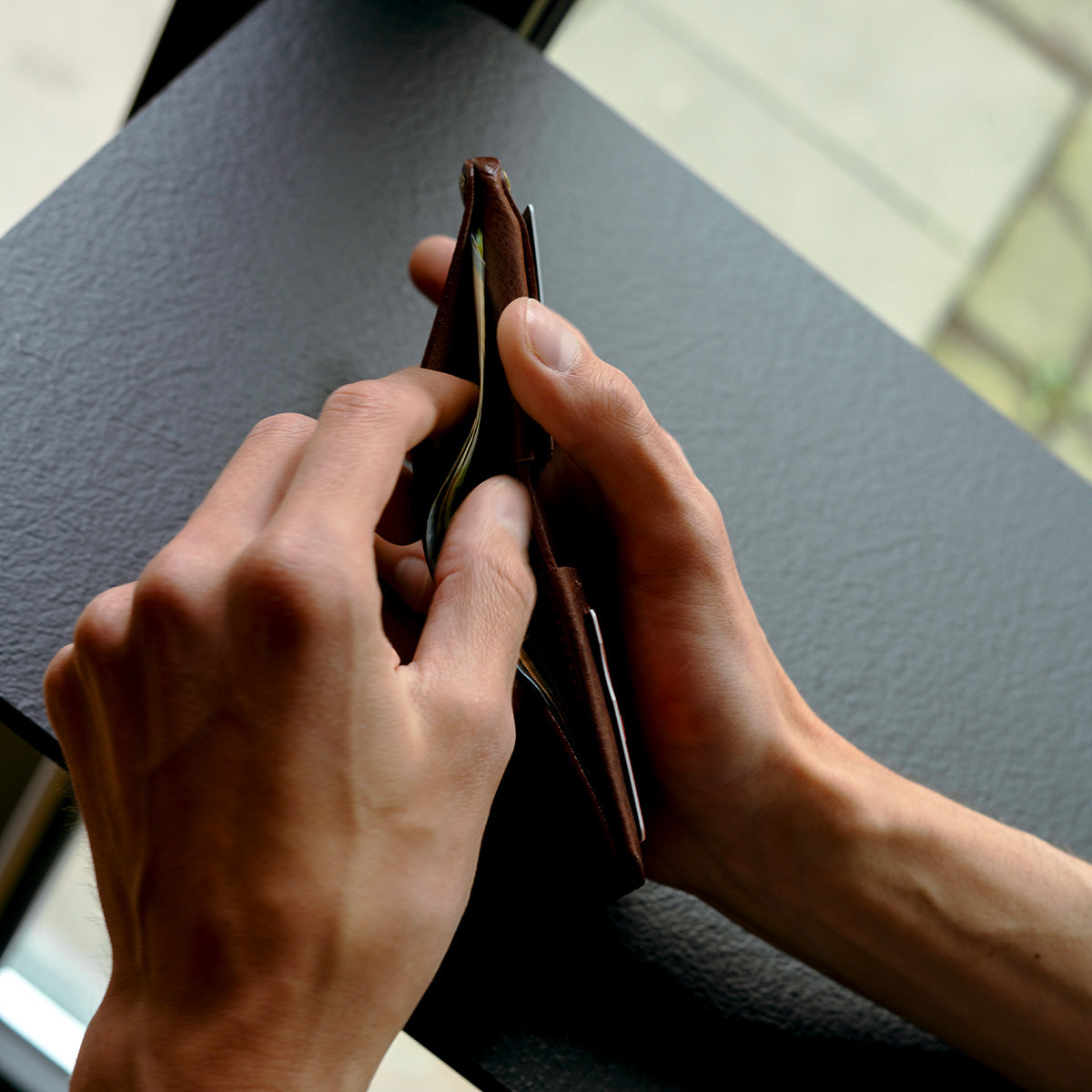 Slim leather AirTag wallet shown from side, holding cards and cash without bulk
