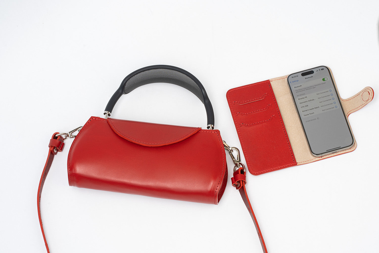 Red leather AirPods Max crossbody case with top handle and long strap next to an open iPhone folio wallet case, flat lay on white background