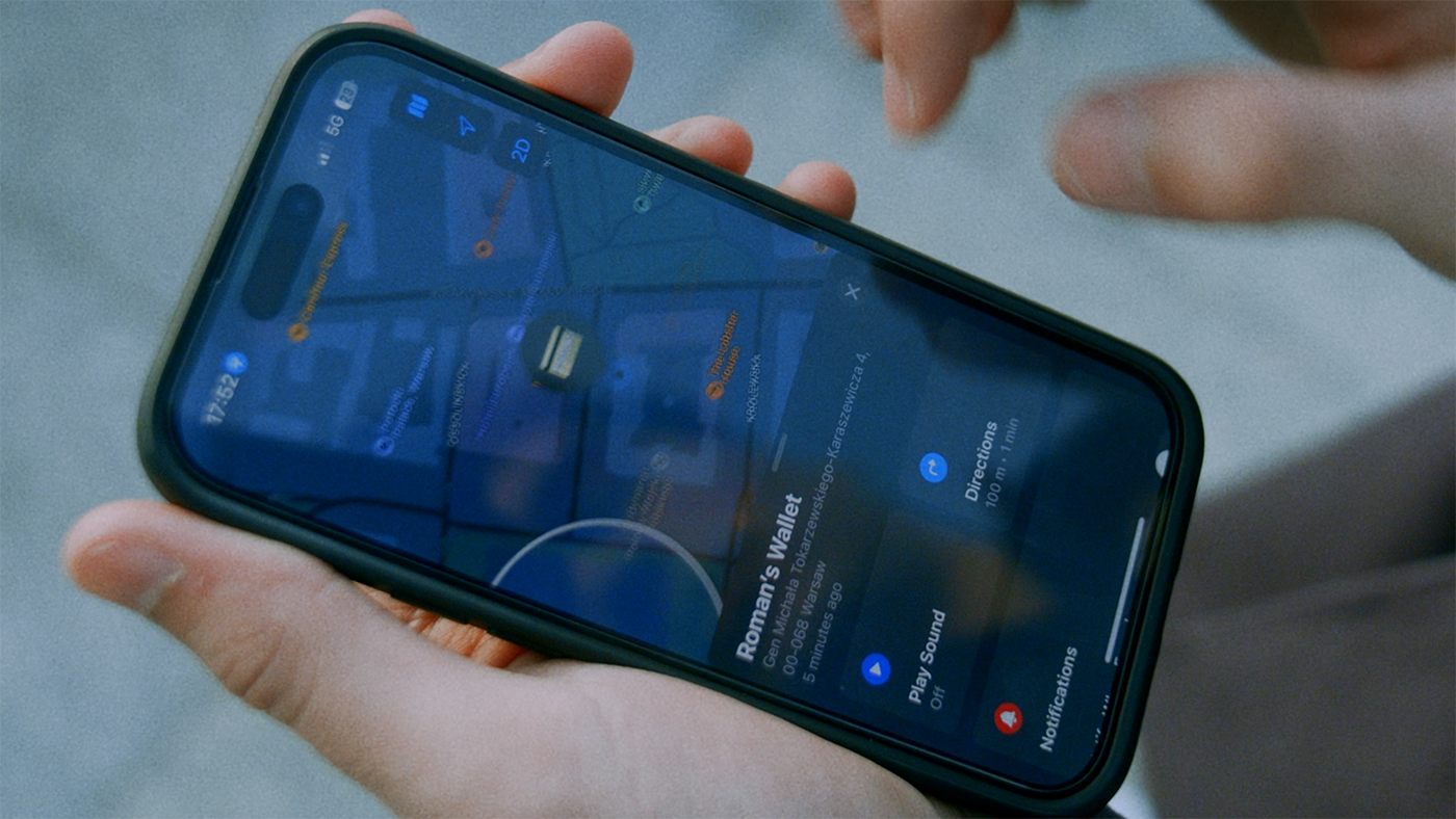 Hand holding an iPhone showing Apple Find My tracking for an AirTag wallet, with location and directions on screen