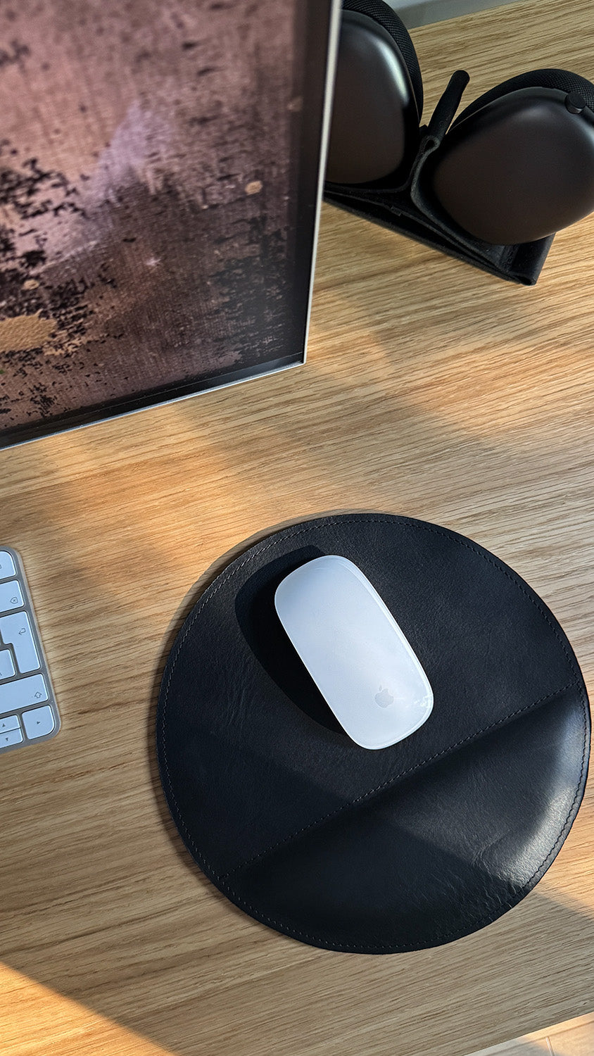 Apple Magic Mouse on round black leather mouse pad on wooden desk