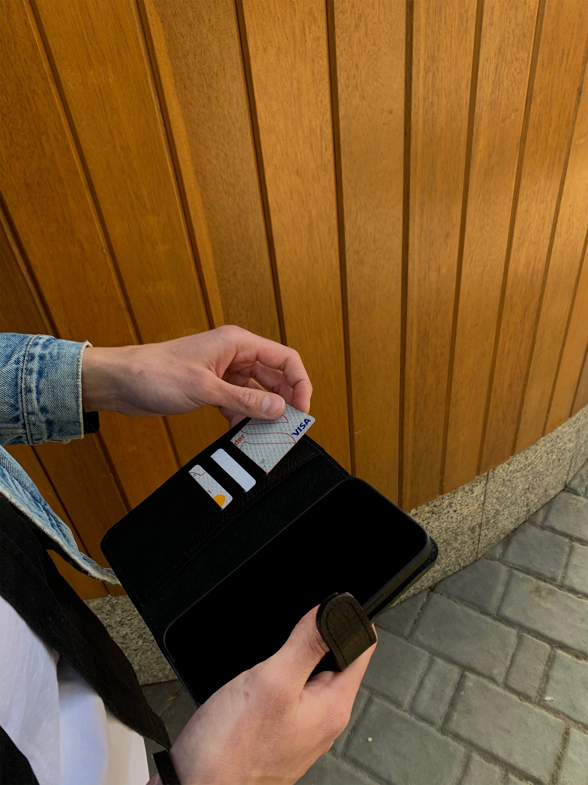 Person taking a card from a black leather iPhone folio wallet case, outdoor lifestyle photo