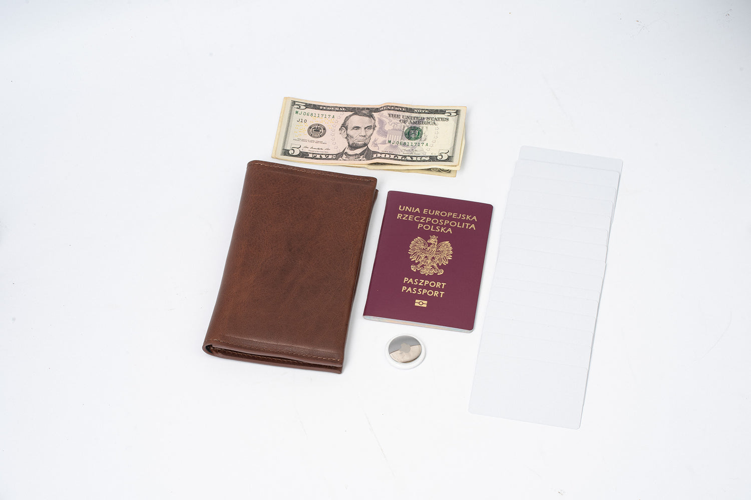 Dark brown leather AirTag passport travel wallet shown with a passport, cash, cards, and an Apple AirTag on a white background to illustrate carry capacity