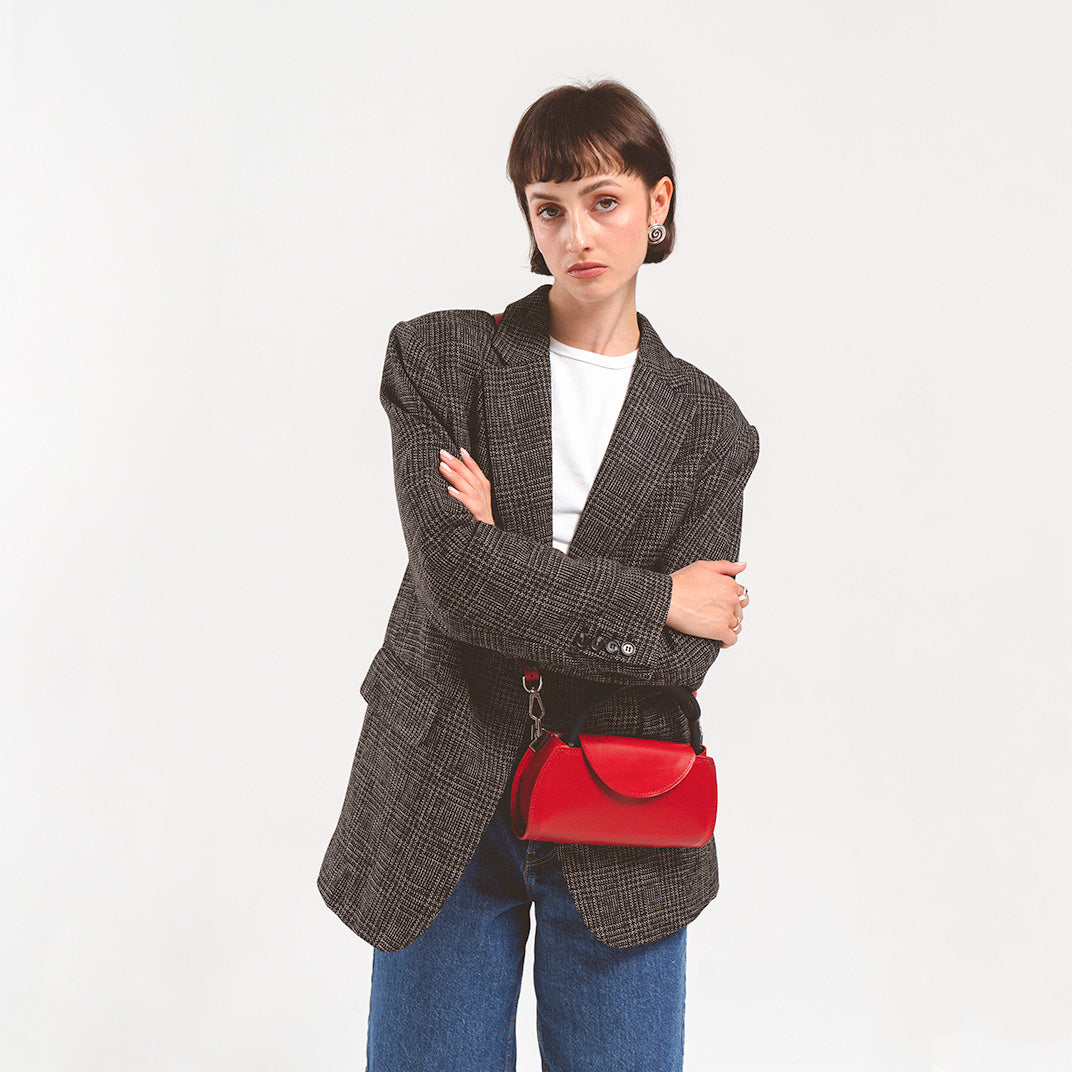 Leather case for AirPods Max in vibrant red, confidently carried by a woman in a textured blazer, adding a pop of color to her ensemble