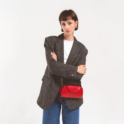 Leather case for AirPods Max in vibrant red, confidently carried by a woman in a textured blazer, adding a pop of color to her ensemble