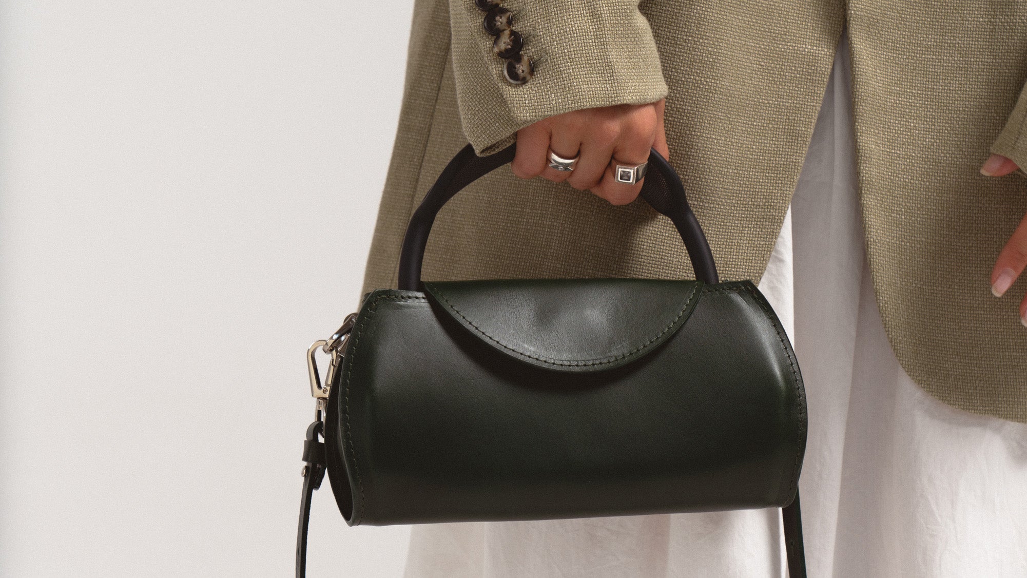 Woman holding a dark green leather AirPods Max case with top handle, close-up lifestyle photo