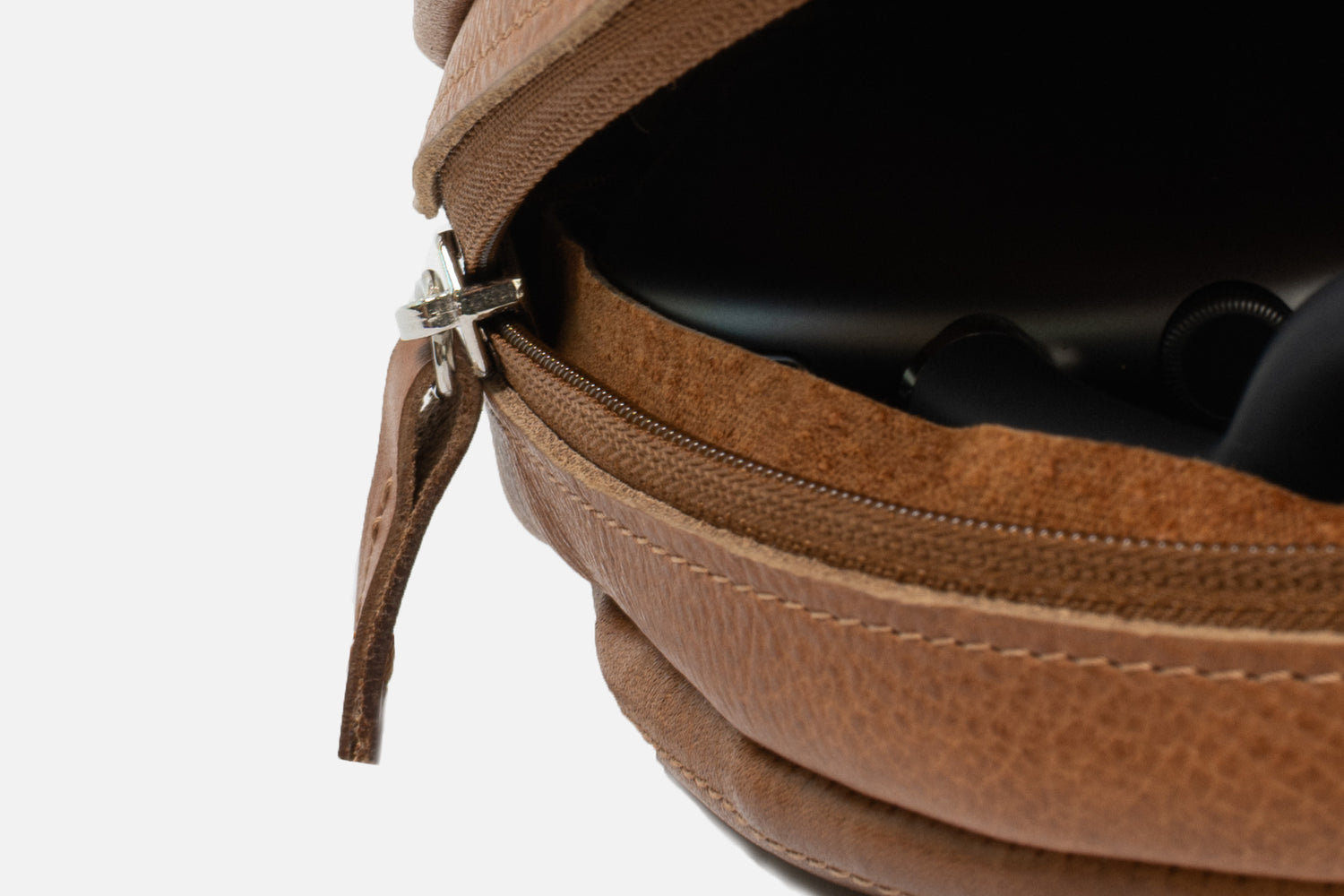 Close-up of tan leather AirPods Max case showing metal zipper, suede lining, and protective padding edge around the headphones inside.