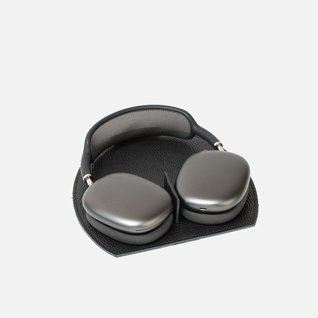 AirPods Max on a black leather rest station with a magnetic tab that triggers low-power mode, on a white background.