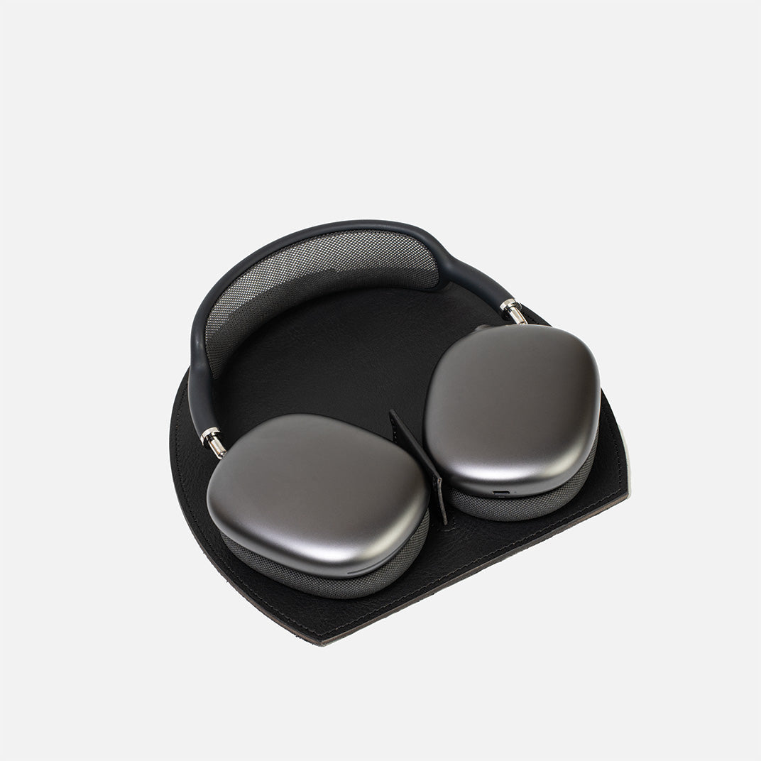 AirPods Max on a black leather rest station with a magnetic tab that triggers low-power mode, on a white background.