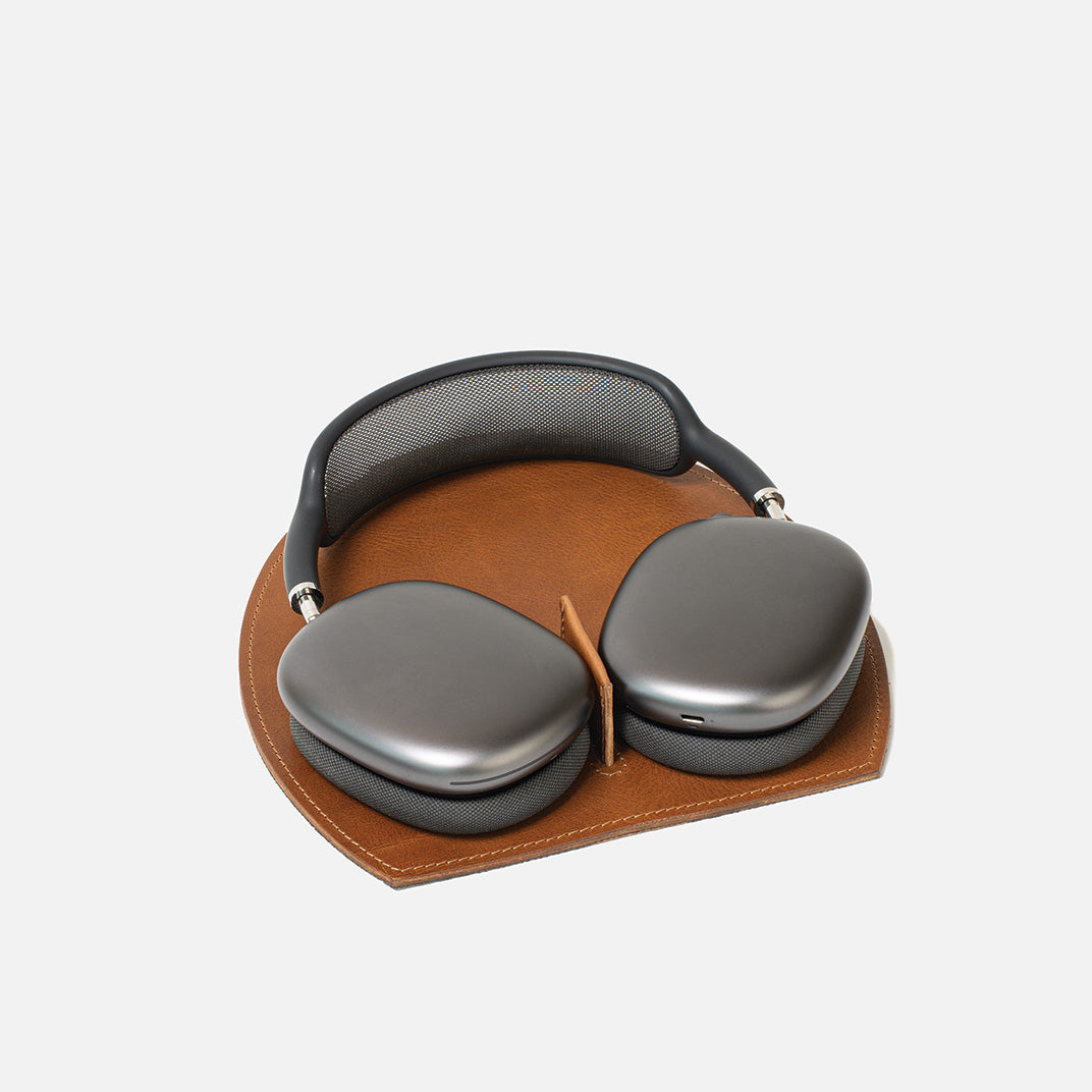 AirPods Max on a brown leather rest station with a magnetic tab that triggers low-power mode, on a white background