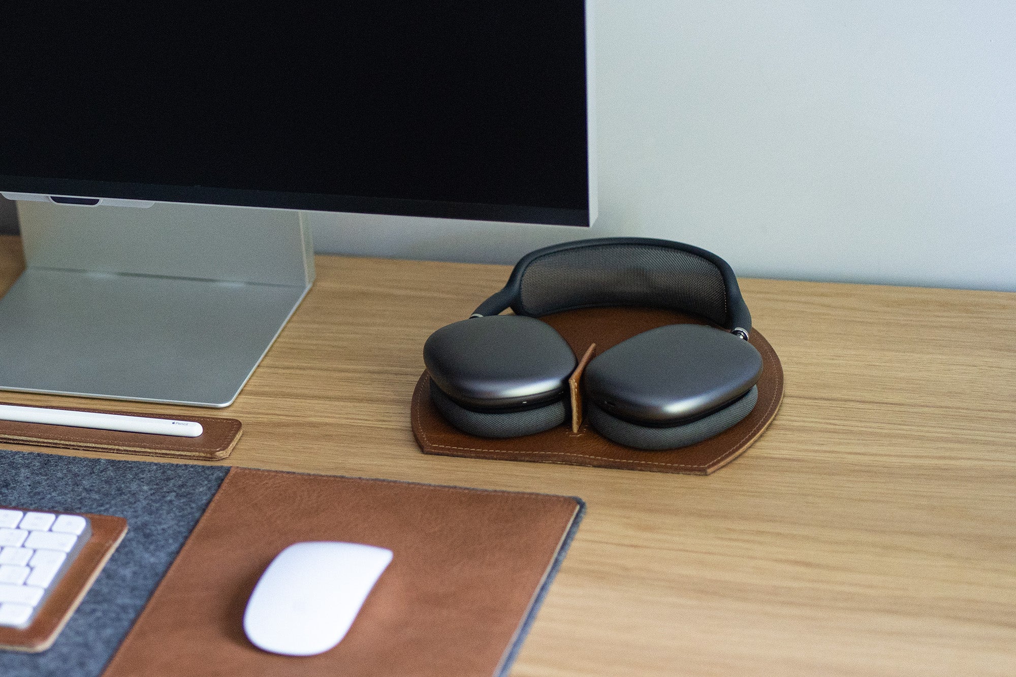 AirPods Max resting on a brown leather desk stand near a computer monitor, workspace lifestyle photo