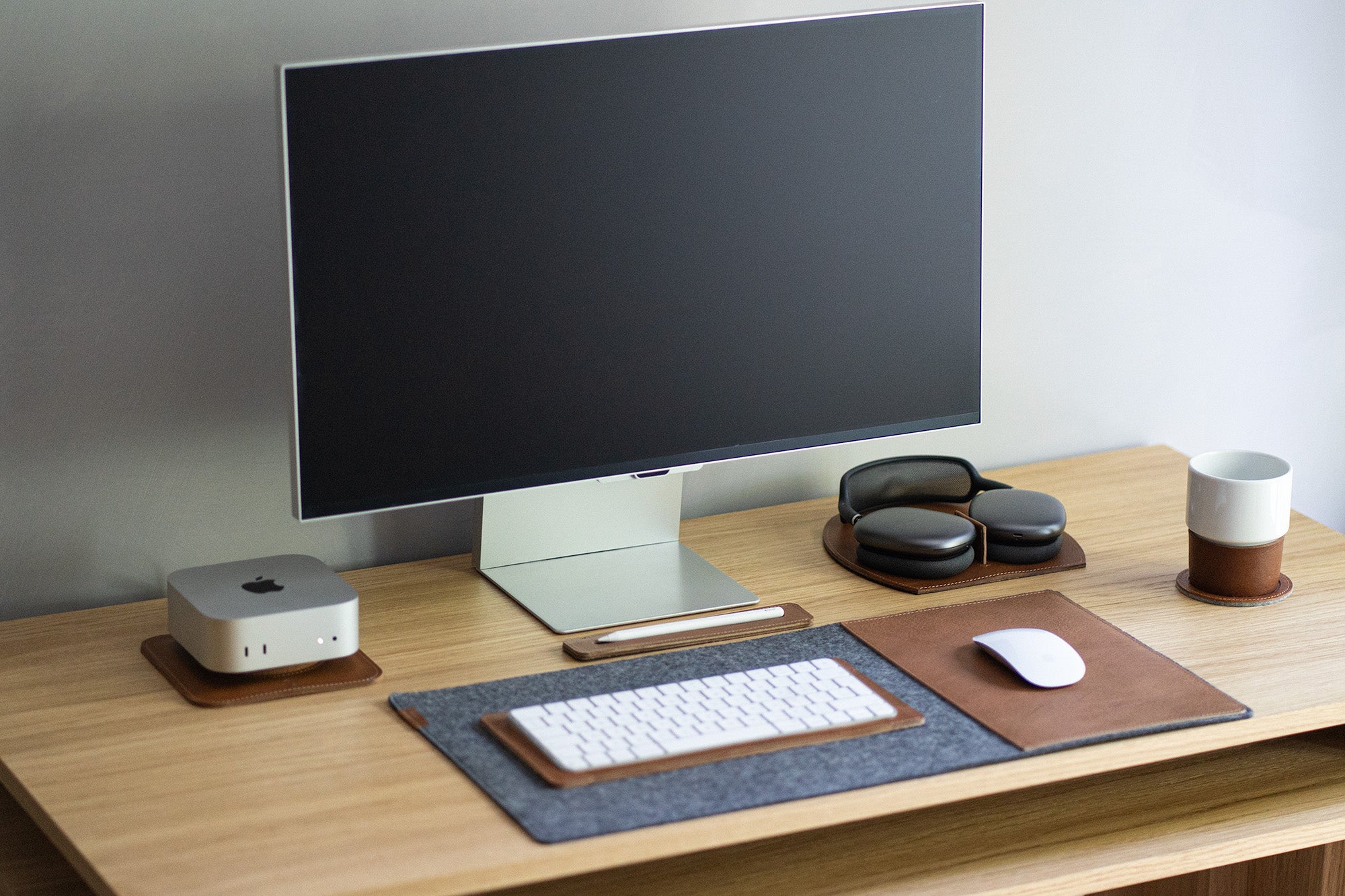 Minimal desk setup with AirPods Max on a brown leather rest station, matching leather accessories, and a computer monitor