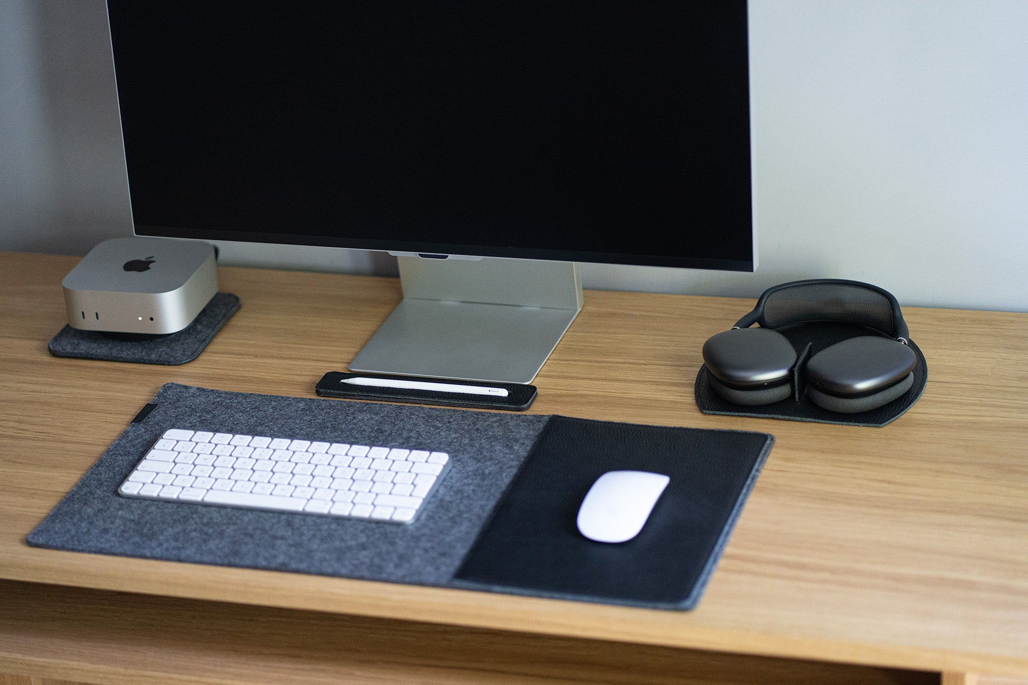 Desk setup with AirPods Max on a black leather rest station, computer monitor, and felt desk mat