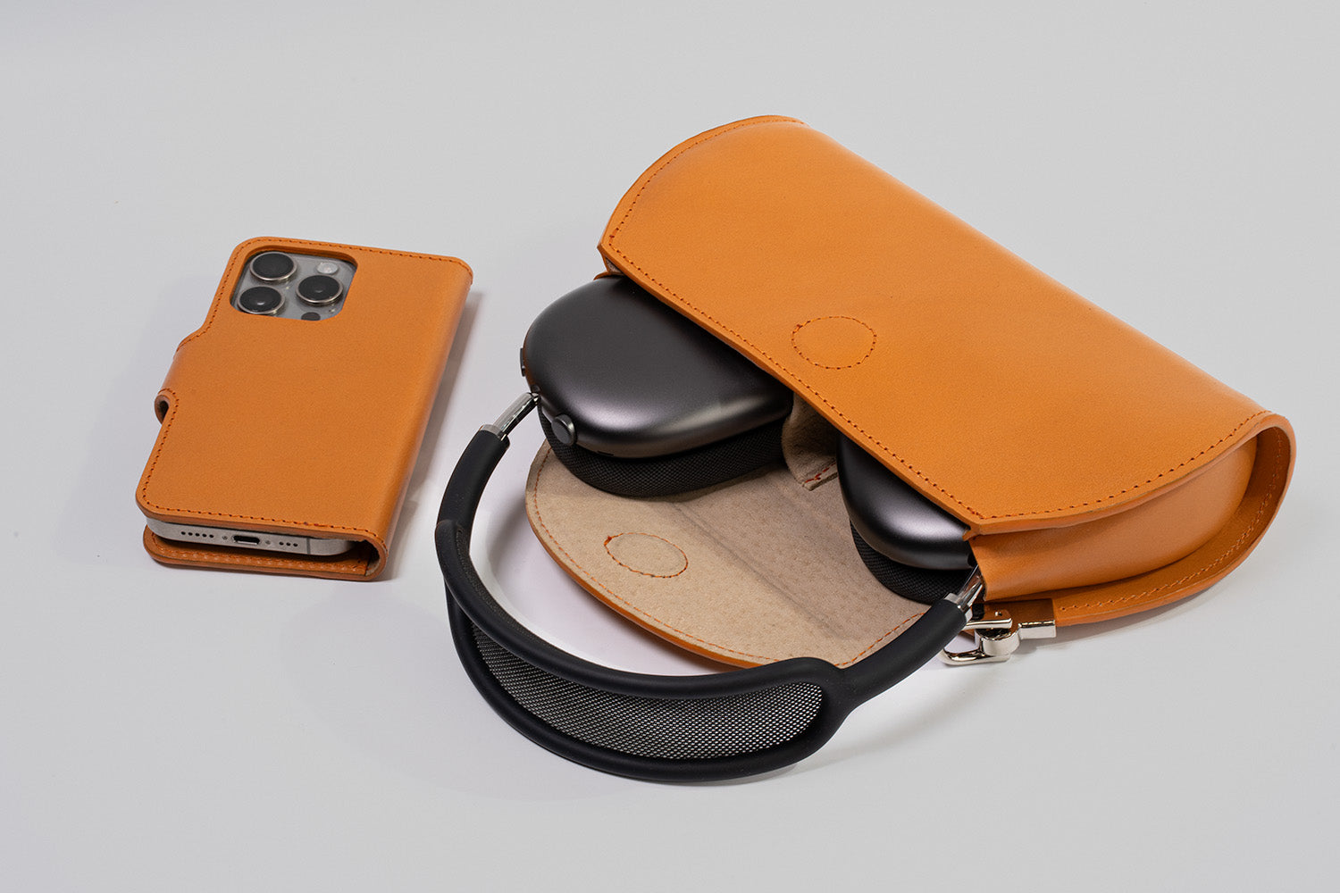 Orange leather AirPods Max case with headphones inside next to a matching iPhone leather folio wallet case, studio flat lay