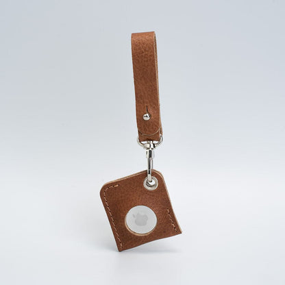 Brown leather AirTag bag charm with a loop strap, angled view showing the white AirTag face.