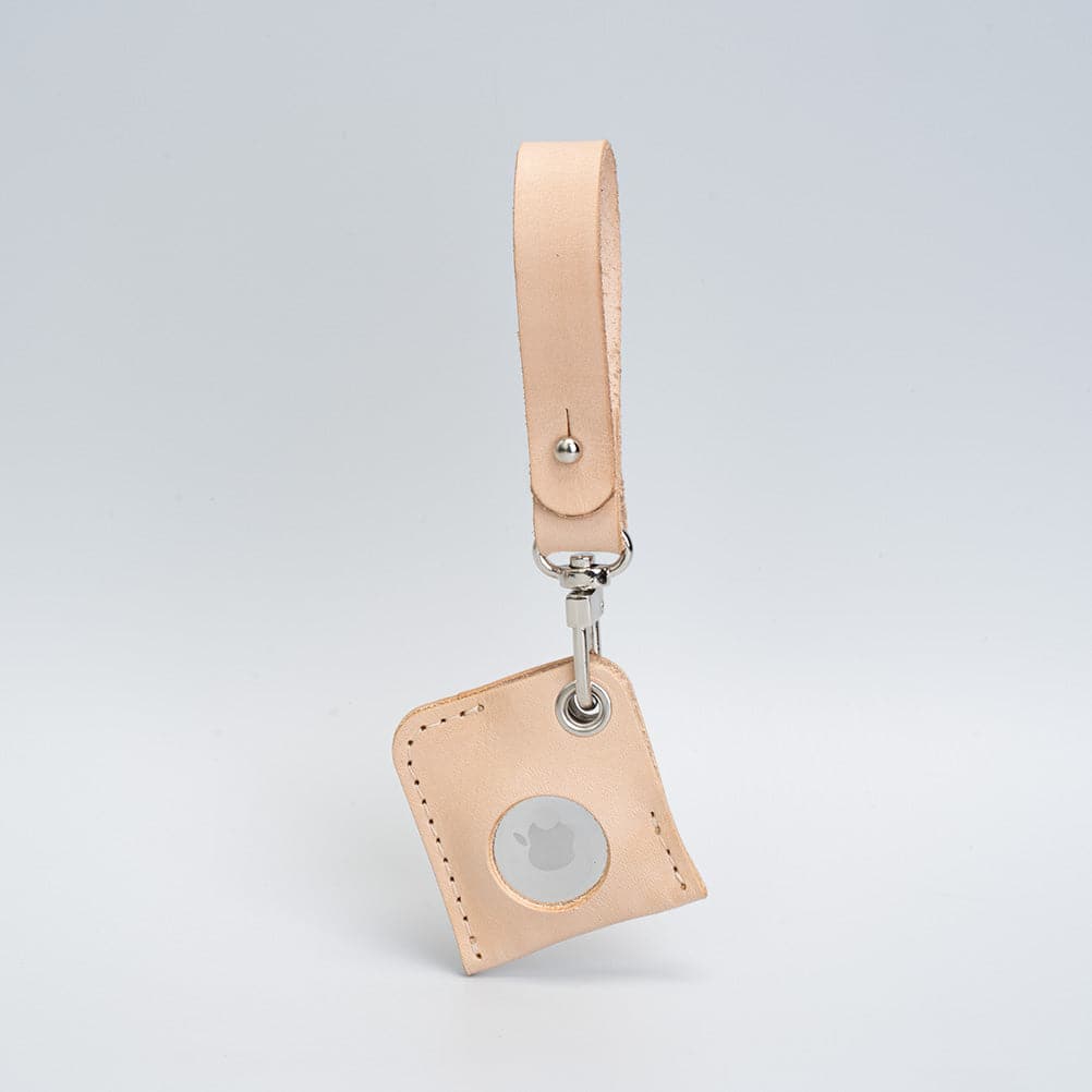 Natural beige leather AirTag bag charm with a loop strap, angled view showing the white AirTag face.