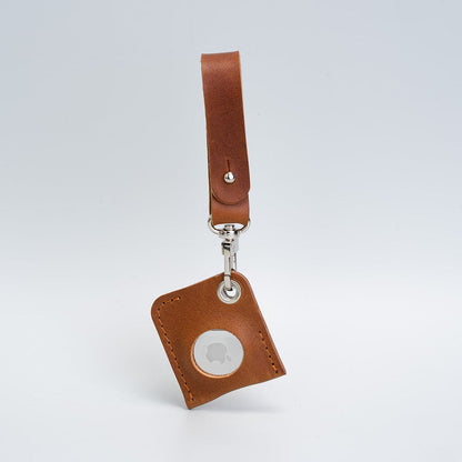 Tan leather AirTag bag charm with a loop strap and silver-tone clasp, angled view on a grey background.