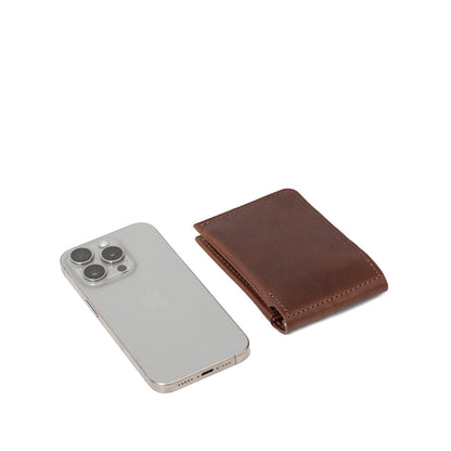 Mahogany leather AirTag money clip wallet for men folded next to iPhone, slim pocket-friendly design – Geometric Goods