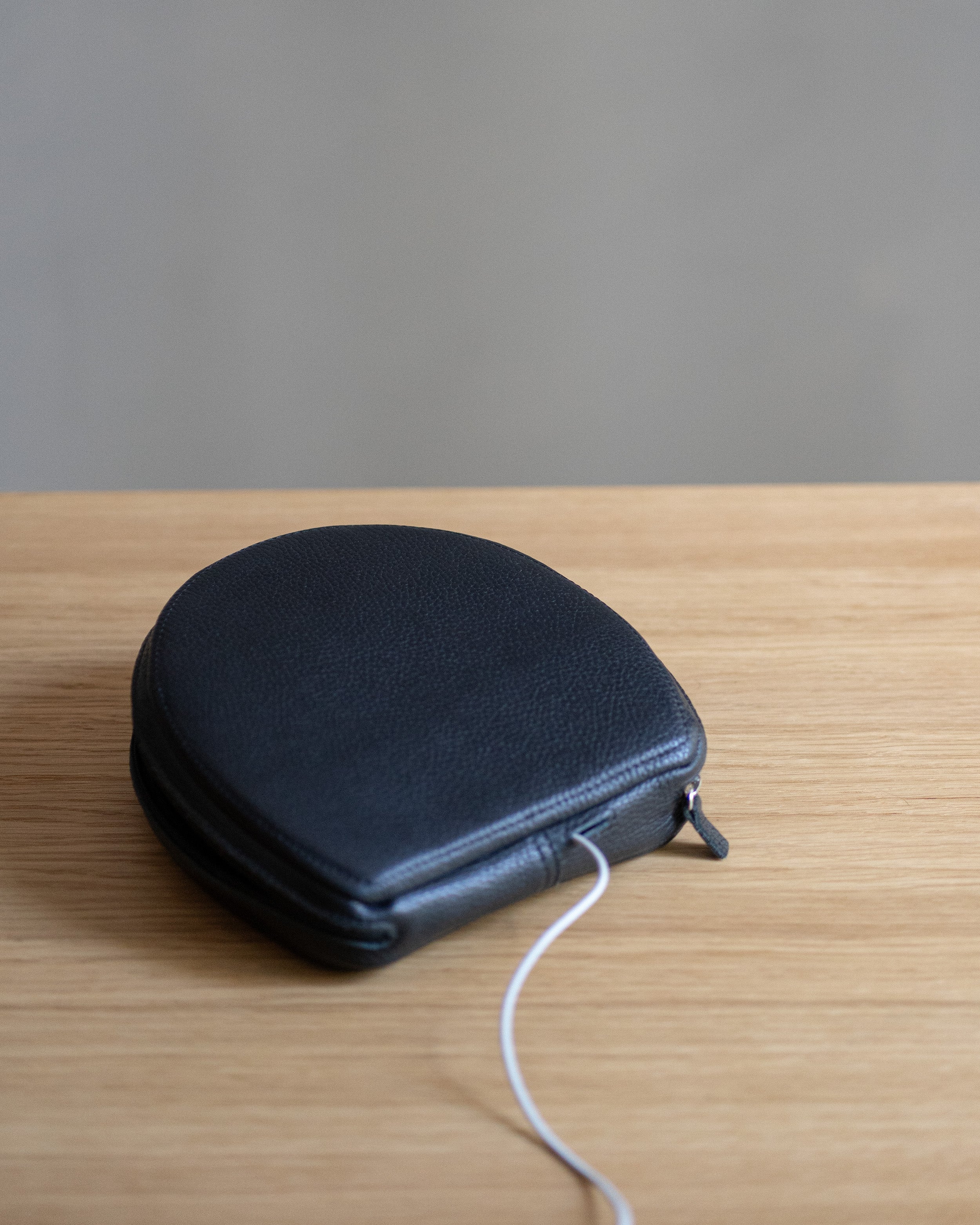 Closed black flat-grain leather case for AirPods Max on a wooden table