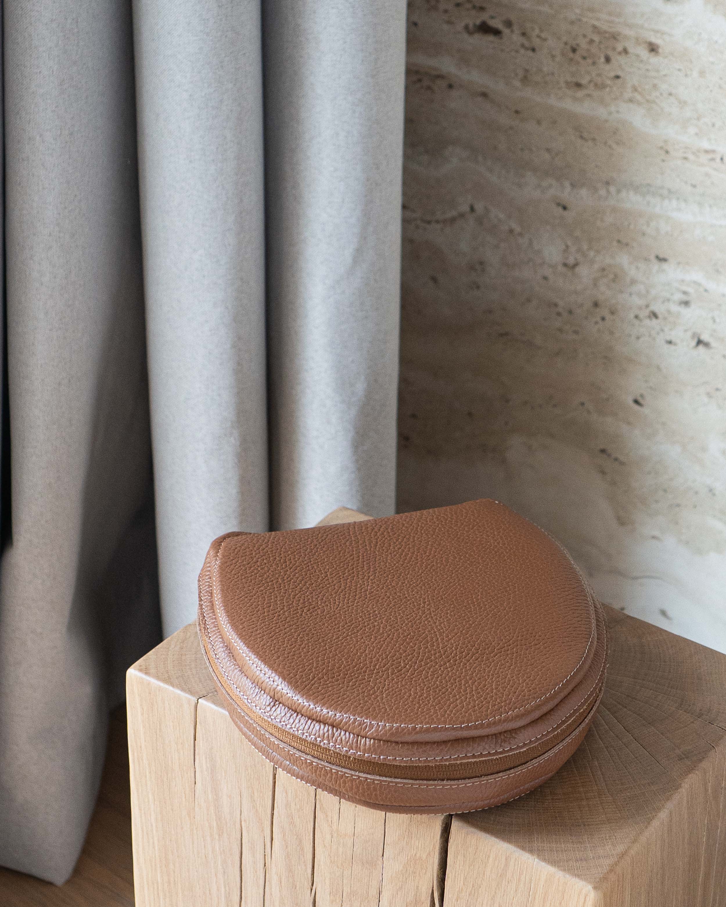 Closed brown flat-grain leather case for AirPods Max on a wooden pedestal