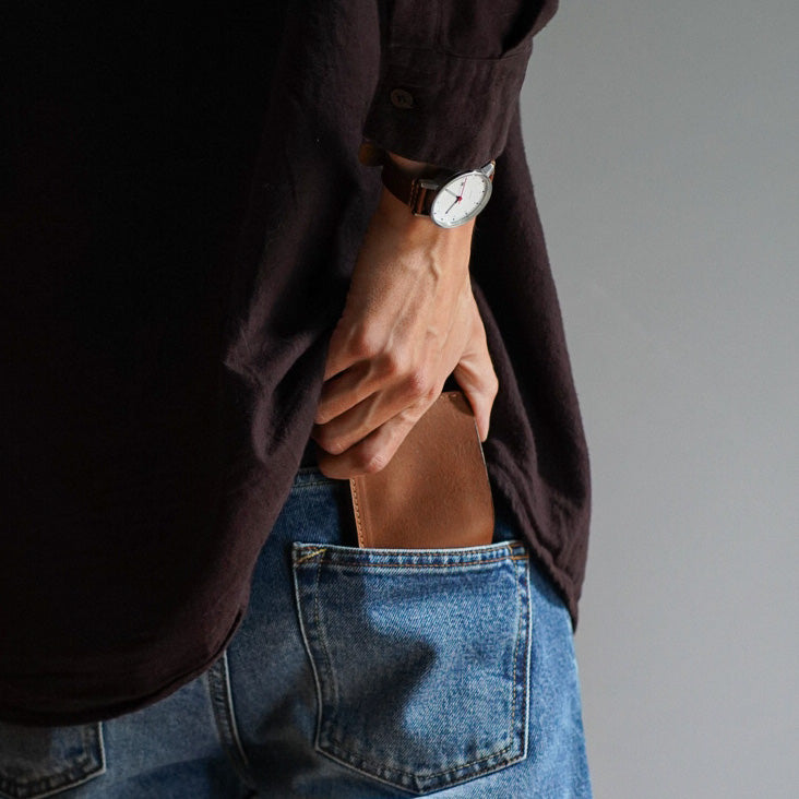 Brown leather wallet being placed into a back pocket of jeans