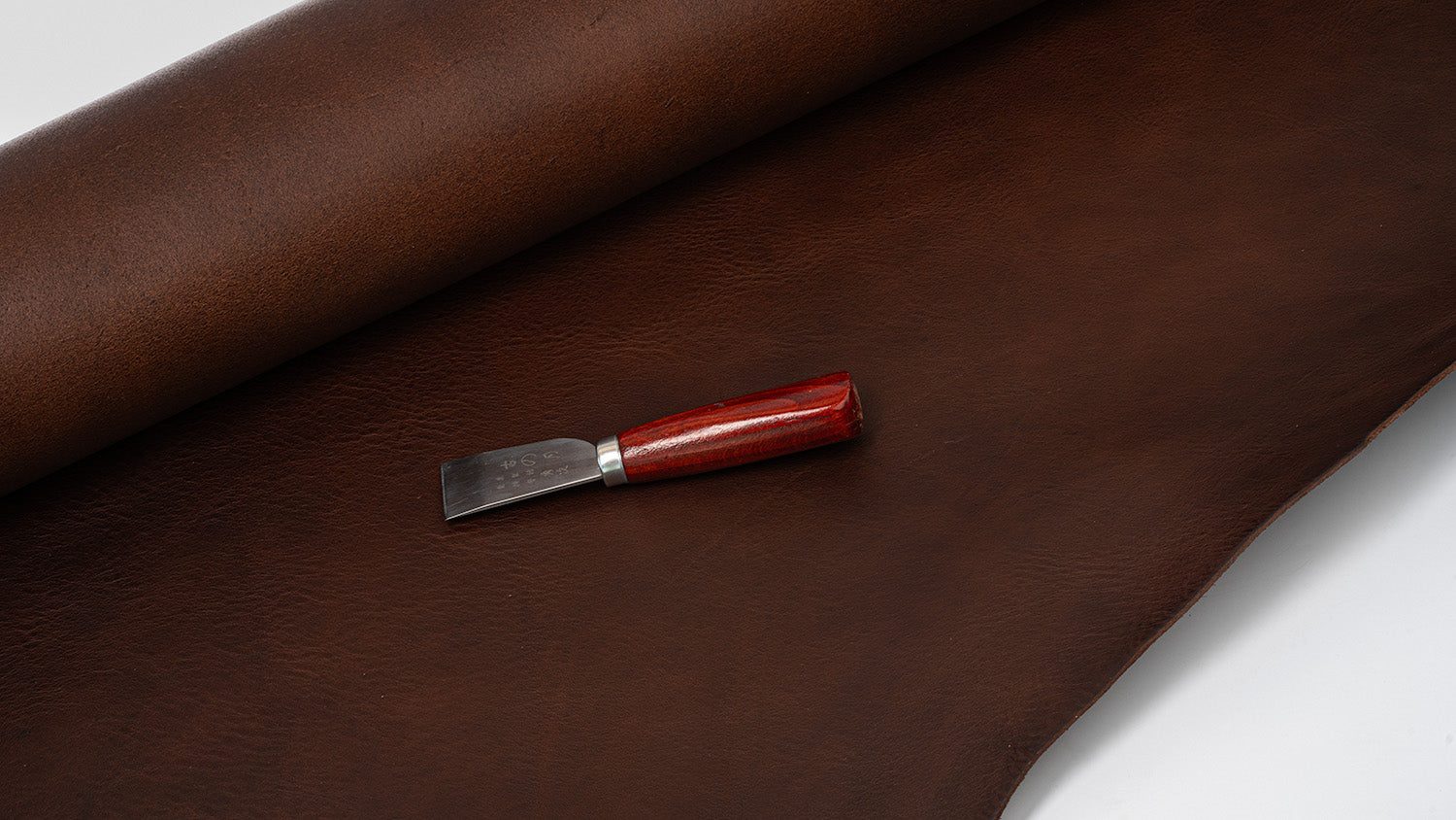 Italian leather hide with leatherworking knife, workshop material flat lay