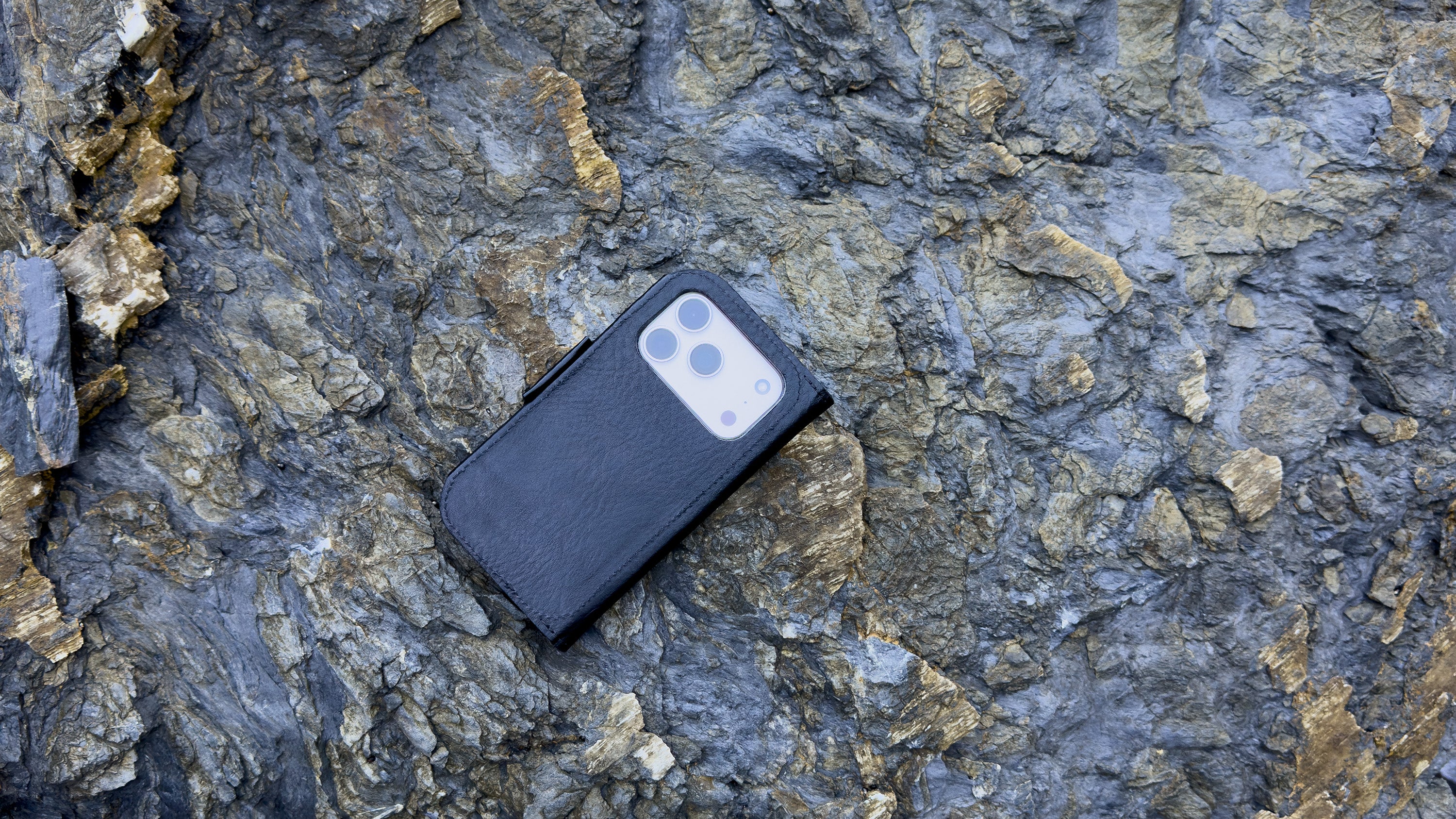 Black leather MagSafe-compatible folio wallet case for iPhone 17, flat lay on rock texture