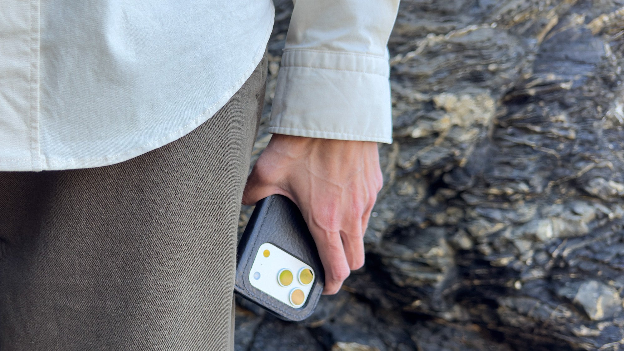 Black leather iPhone 17 folio wallet case carried in hand, lifestyle photo outdoors