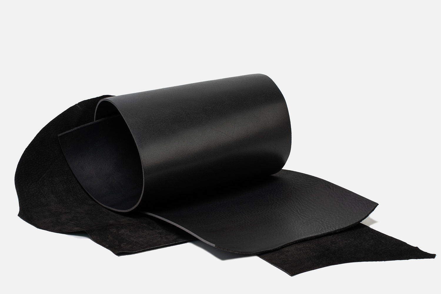 Black Italian vegetable-tanned leather hide with suede underside, rolled and laid flat on a white background