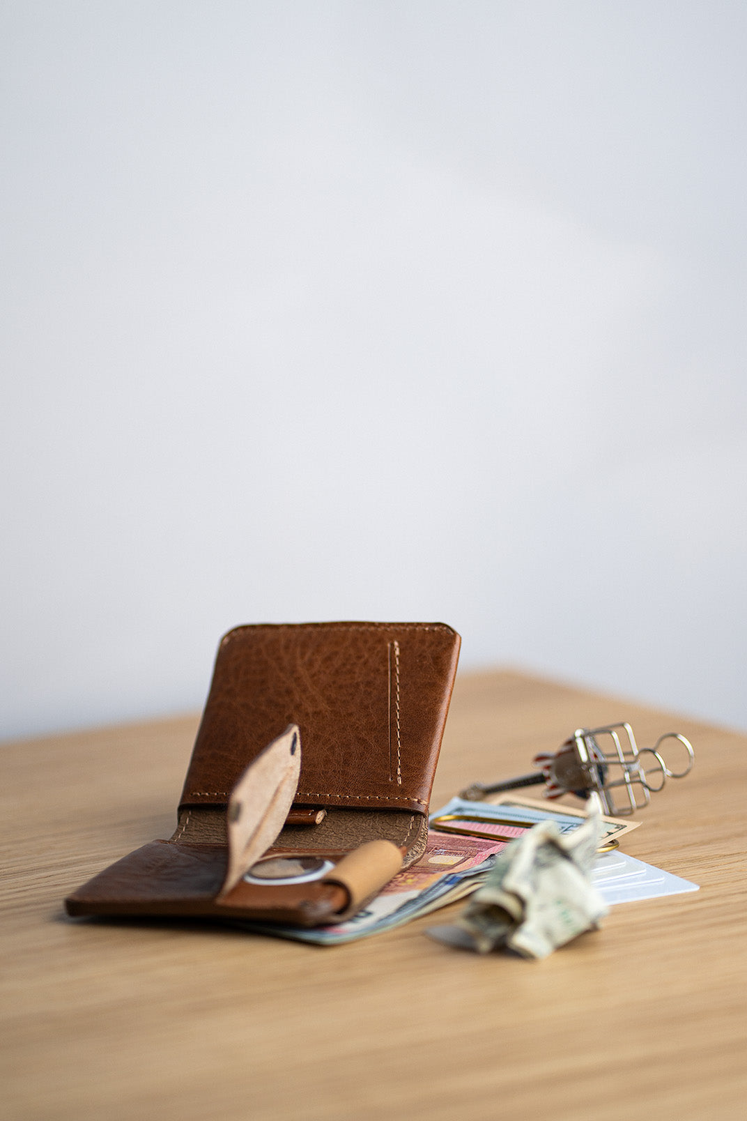 Brown leather airtag wallet with money and keys on a wooden surface