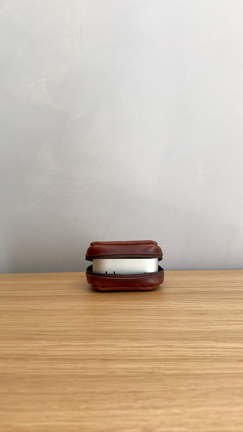 Open brown leather case on a wooden surface with a compact silver device partially visible inside
