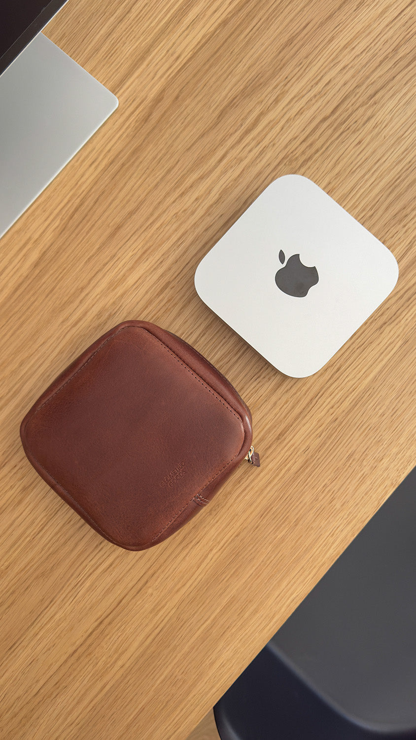 Brown leather zippered case on a wooden desk beside a compact silver desktop computer mac mini