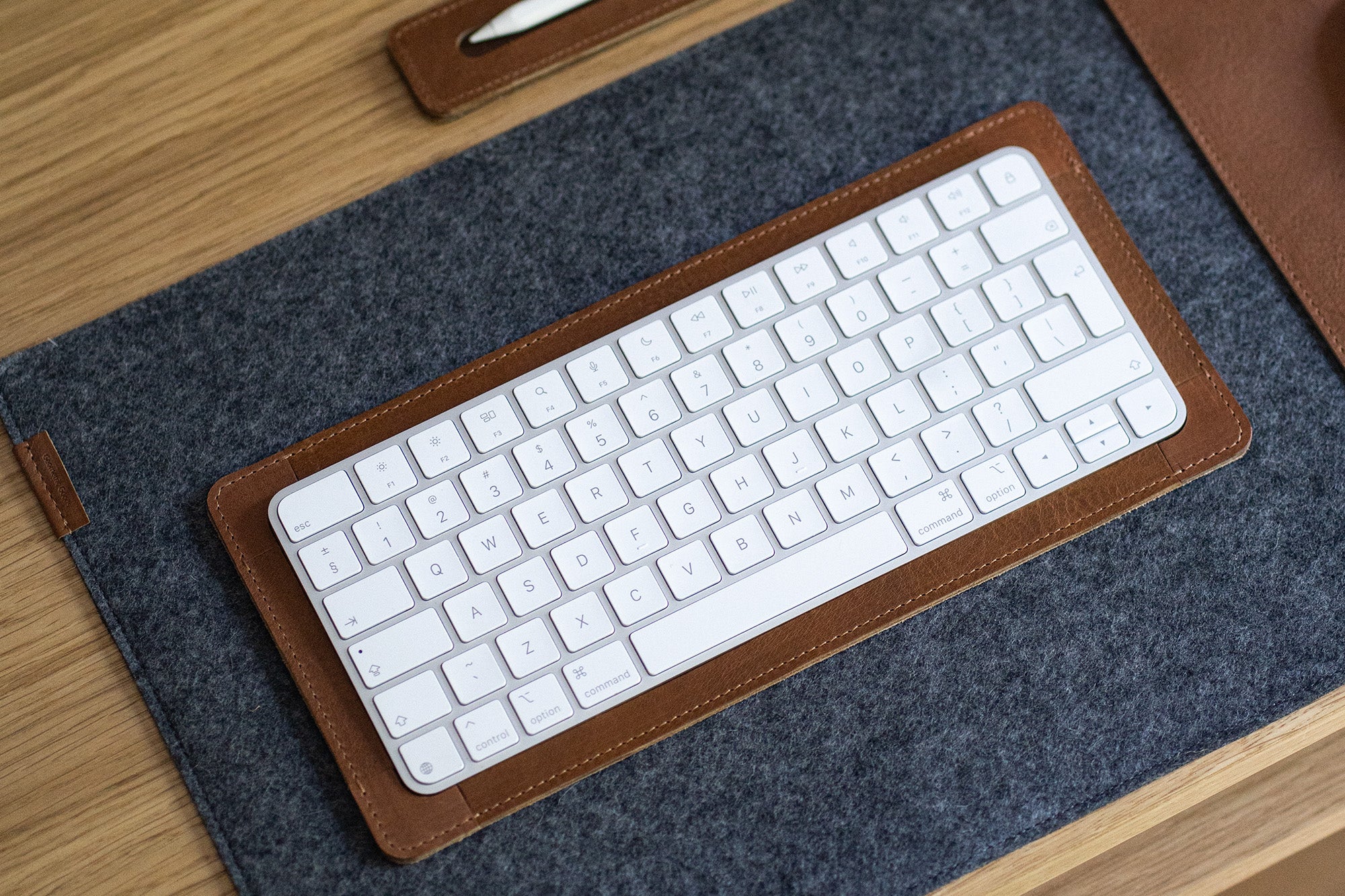 White wireless keyboard resting in a brown leather tray on a gray felt desk mat, viewed from above.