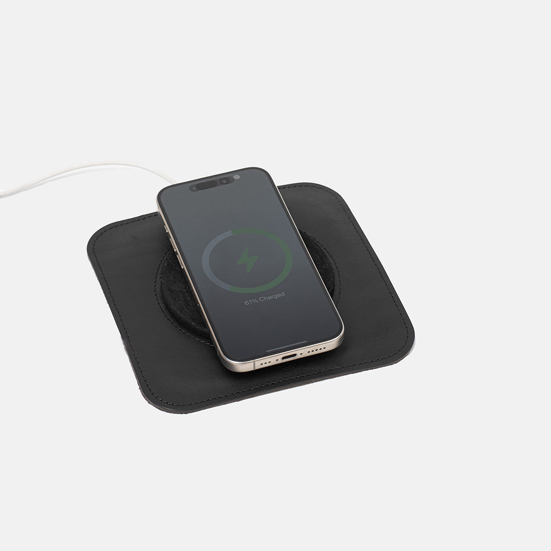 Black Italian leather MagSafe charging mat with iPhone placed on top, minimalist wireless charger pad