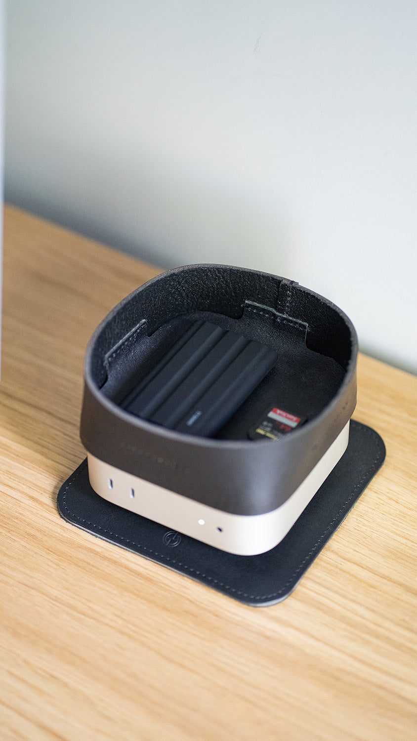 Mac mini desktop computer with a leather tray placed on top, on a wooden desk