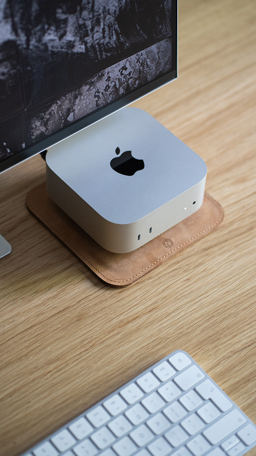 mac-mini computer placed on a leather stand on a wooden desk, top-angle view with keyboard and monitor nearby