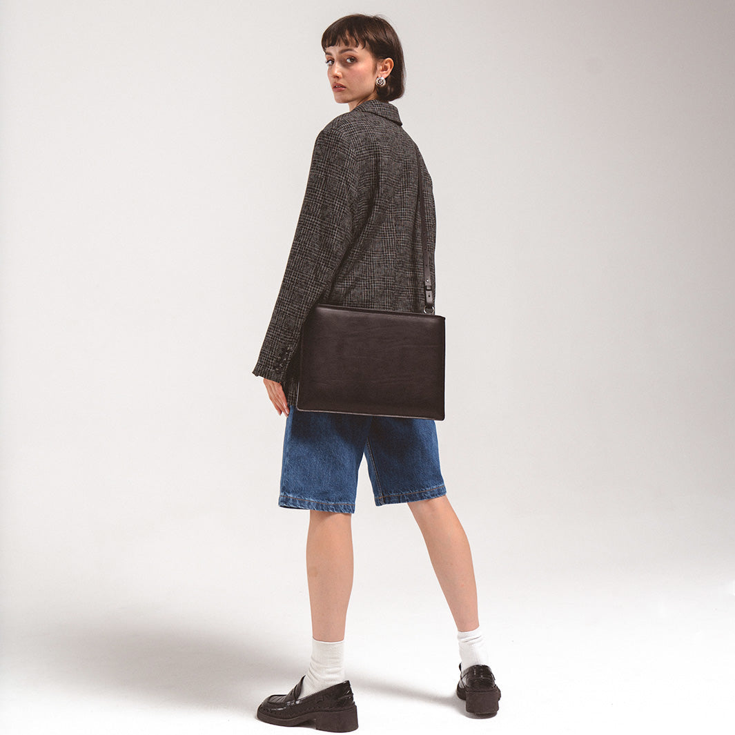 MacBook sleeve - Slim leather sleeve with adjustable strap worn by a woman in a black blazer and denim shorts