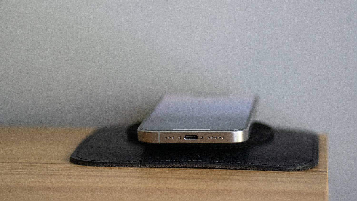 Side view of a smartphone resting on a black magsafe charging leather desk mat