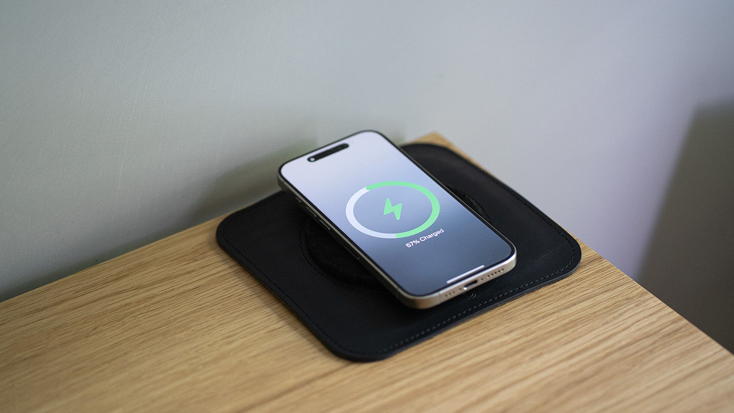 Smartphone resting on a black leather MagSafe-compatible desk mat with charging indicator visible