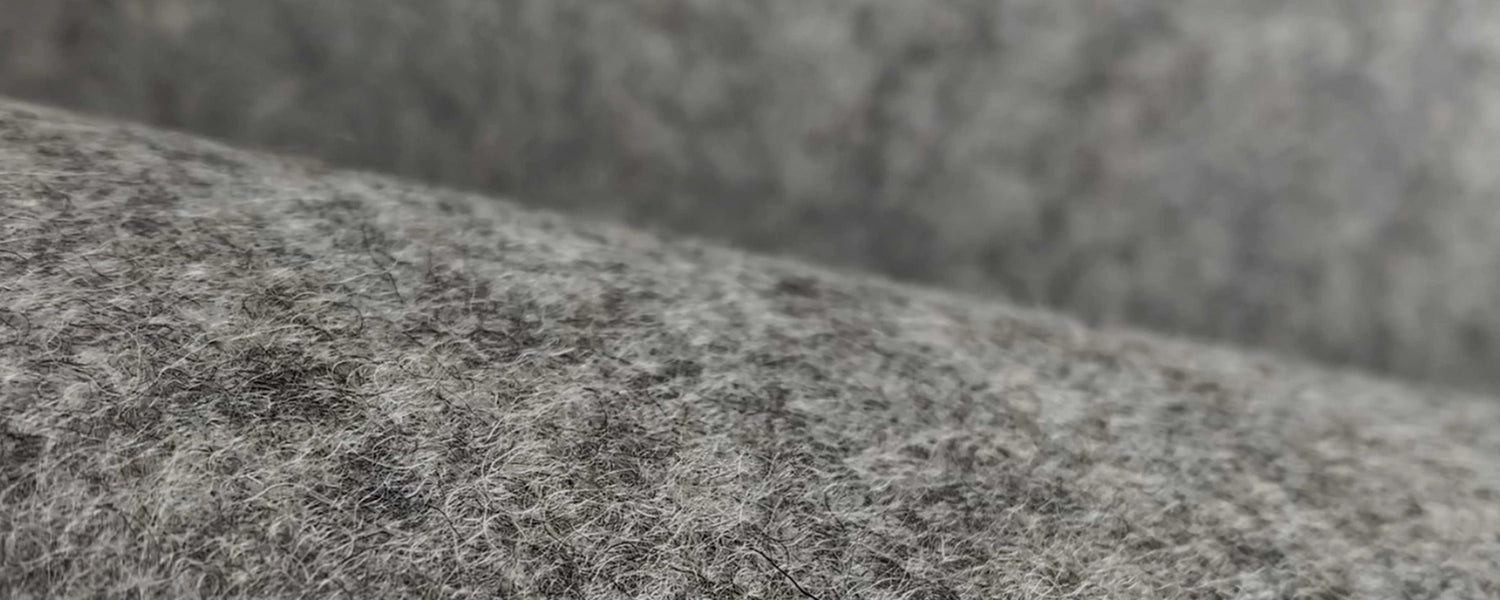 Close-up macro of mottled heather-gray merino wool felt with visible soft fibers and natural speckling across the surface.
