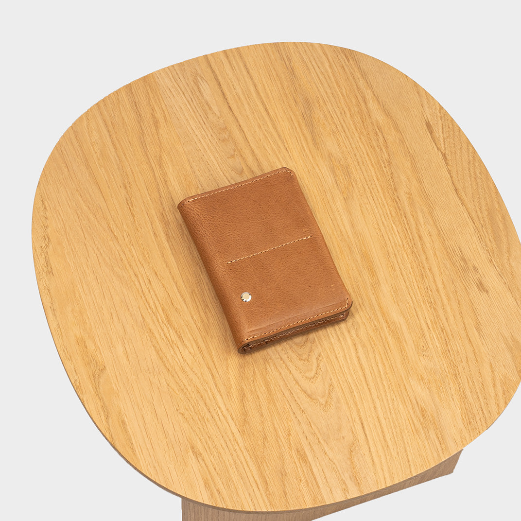 Closed leather travel wallet with hidden AirTag pocket, photographed on a round wooden table to show compact size